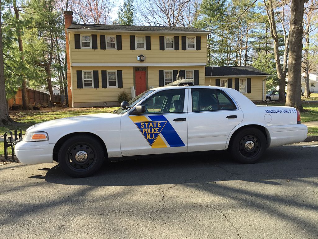 Photo of white New Jersey police department state police car outside a house. Taken from Wikimedia Commons.