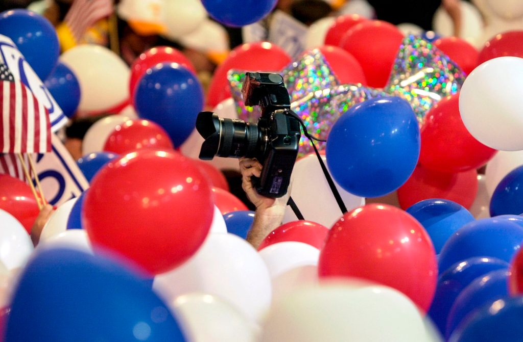 This is a photo of red, white, and blue balloons at the Democratic National Convention in 2000. There is a photojournalist in the middle holding up a camera.
