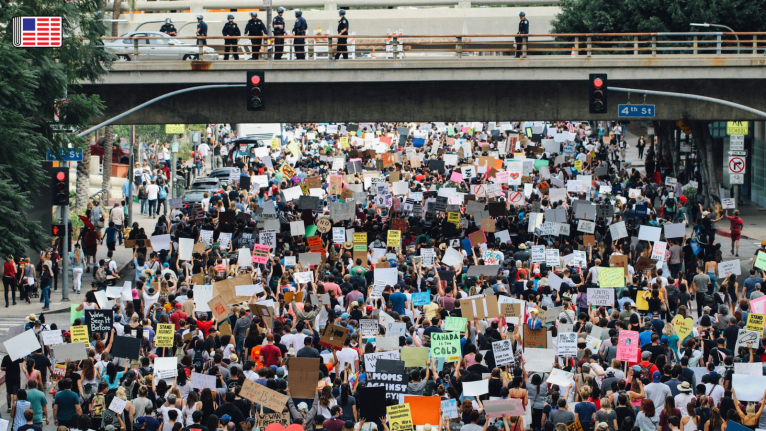 A street full of protesters holding signs while police monitor from above on a bridge. On the top left corner, the Reporters Committee flag logo is shown.