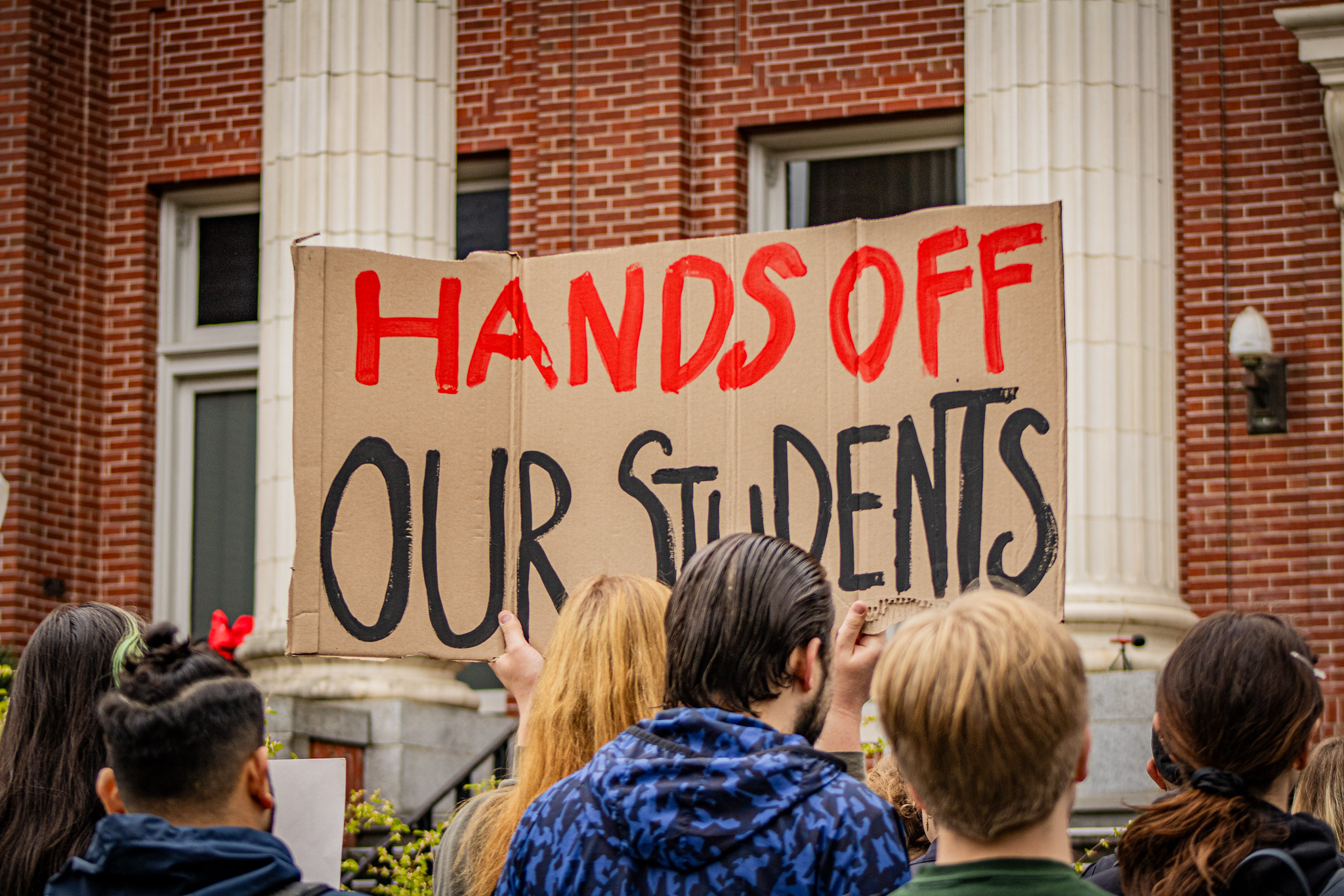 Students at the University of Oregon protest the Trump administration's immigration enforcement actions targeting students. One student holds a sign stating, "Hands off our students."